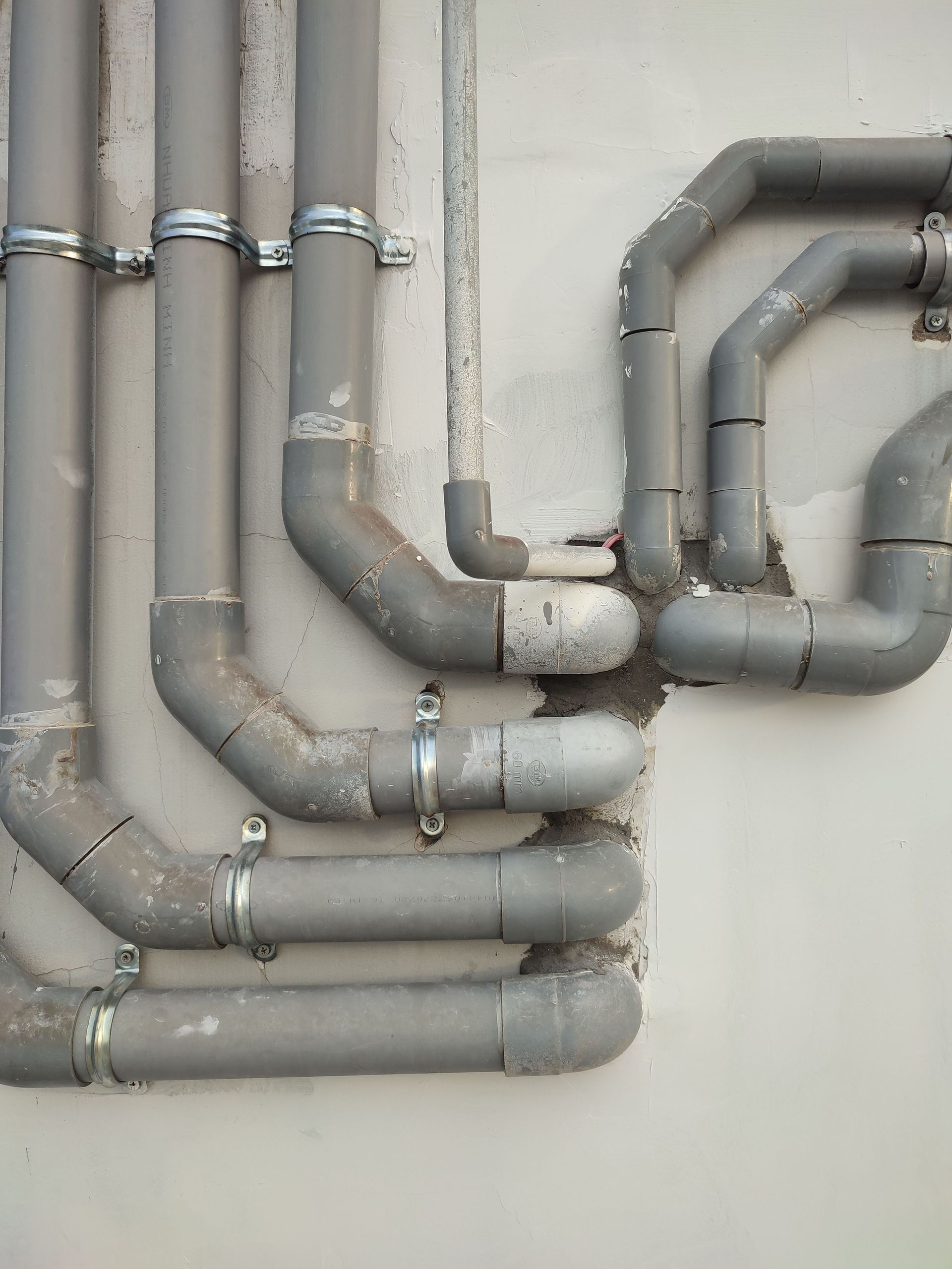 Close-up of interconnected gray metal pipes on an outdoor wall showcasing industrial design.