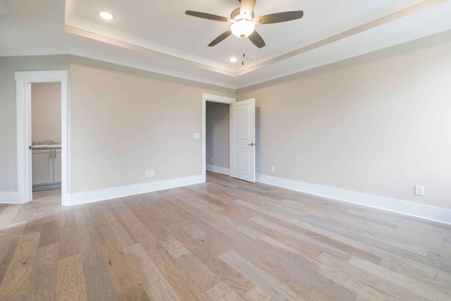 Bright empty room with wooden floors, ceiling fan, and open doors.